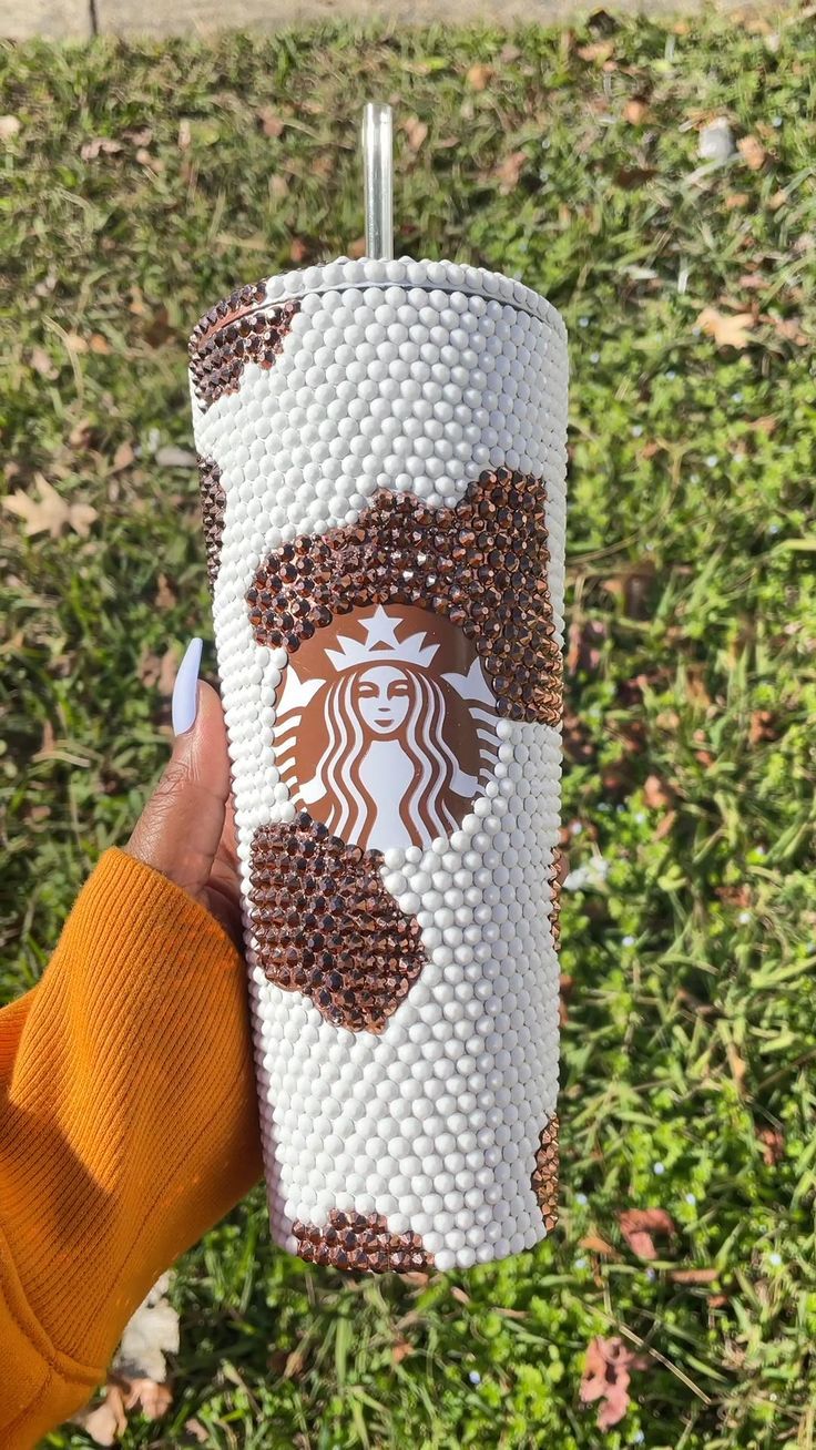 a woman holding up a starbucks cup in her hand with coffee beans all over it