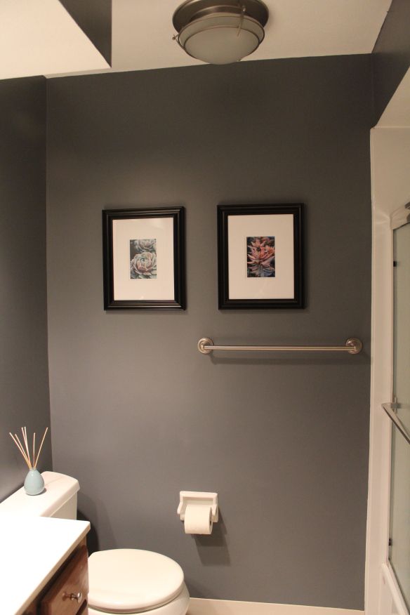 a white toilet sitting next to a bathroom sink under two framed pictures on the wall