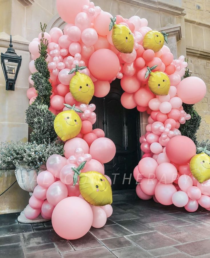 an arch made out of balloons with lemons on top and pink balls around it