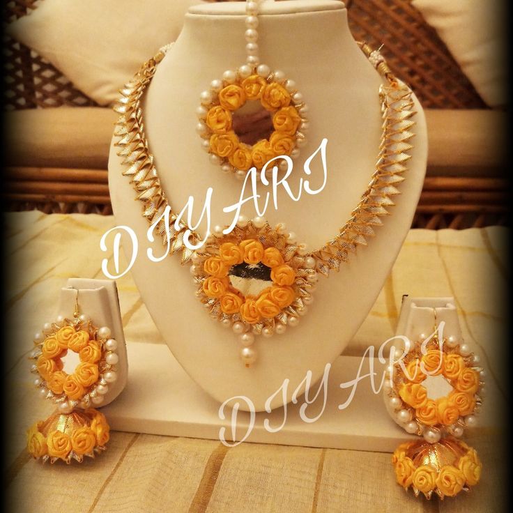 a necklace and earring set made out of orange flowers on a white display stand