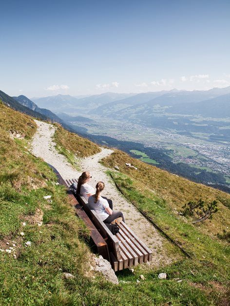 two people sitting on a bench at the top of a hill