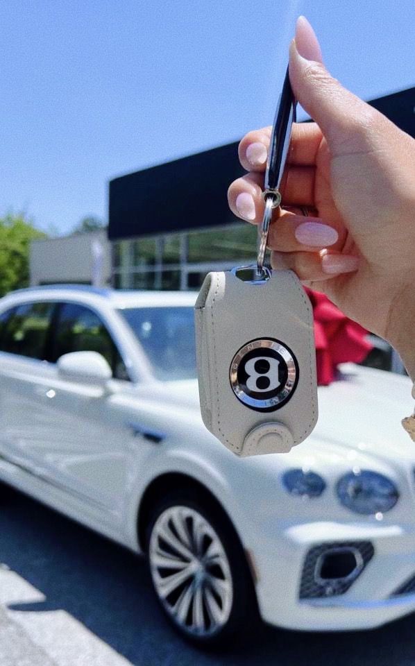 a hand holding a car key in front of a white bentley - benz dealership