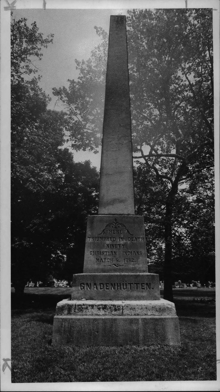 an obelisk in the middle of a grassy area with trees behind it and a sky background