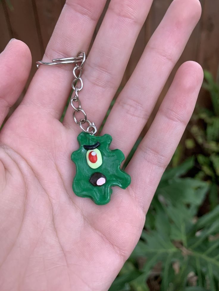 a hand holding a green keychain with a red and black eye on it