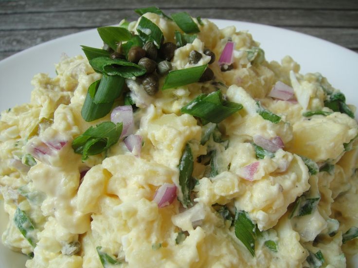 a white plate topped with potato salad on top of a wooden table