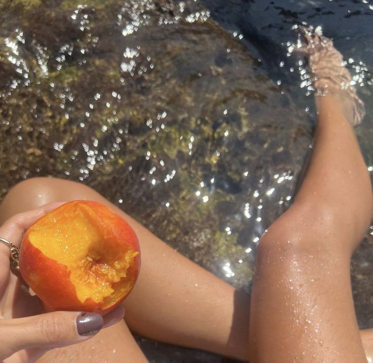 a woman is laying on the beach with an apple in her hand and water behind her