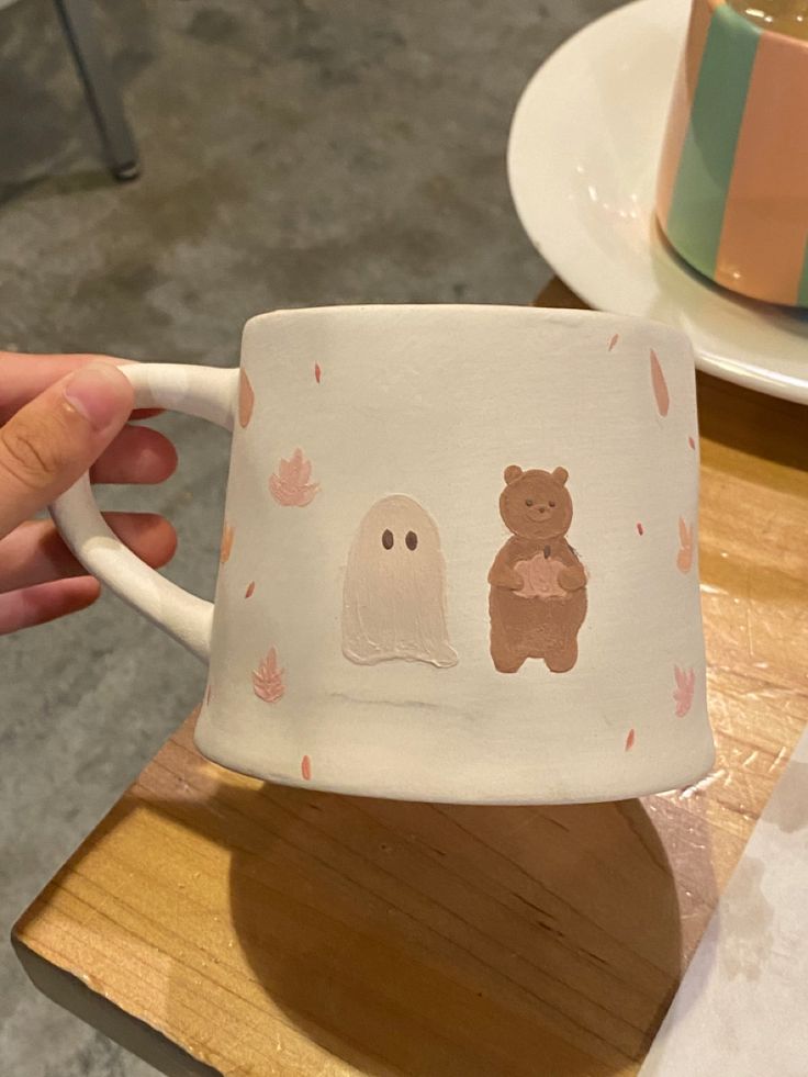 someone is holding up a cup with ghost and bear designs on it while sitting at a table