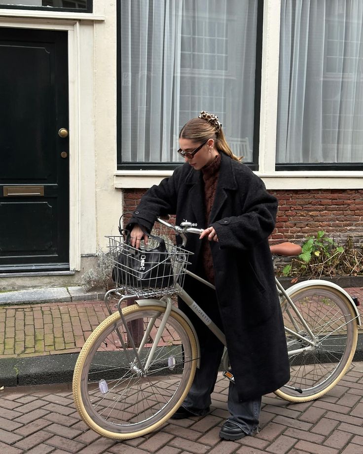 a woman standing next to a bike on the street with a basket in front of her