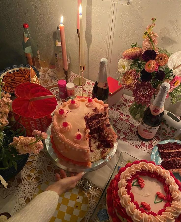 a table topped with cakes and candles next to bottles of wine on top of it