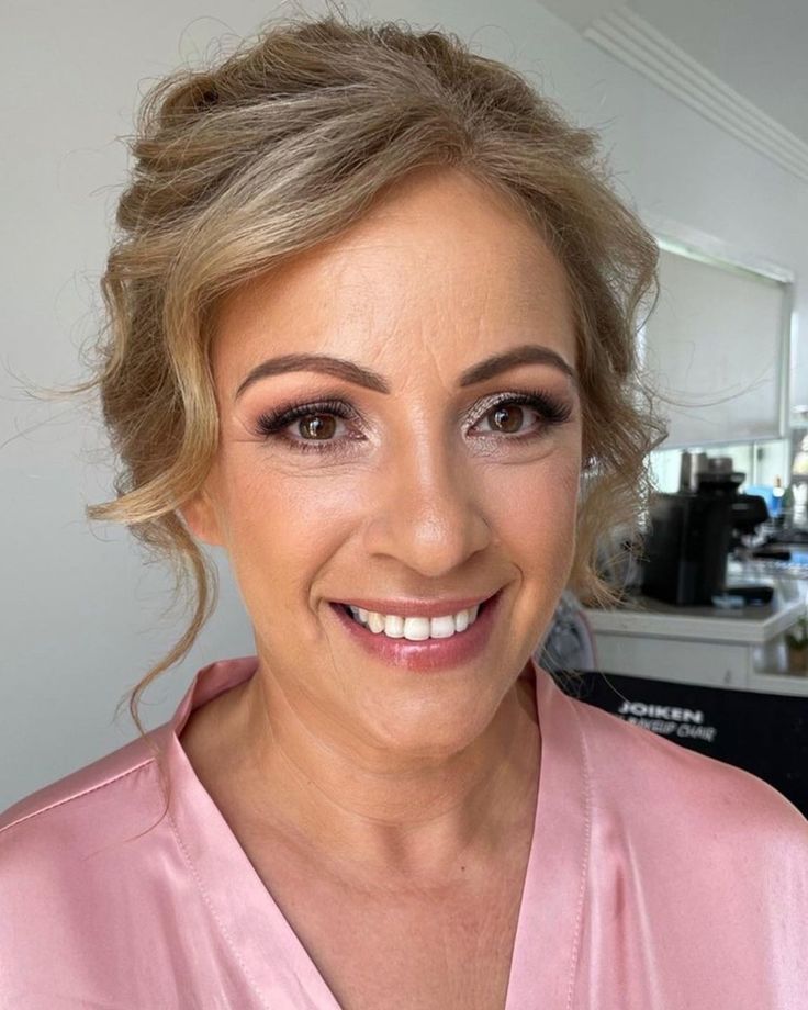 a woman with blonde hair wearing a pink robe and smiling at the camera while standing in front of a mirror