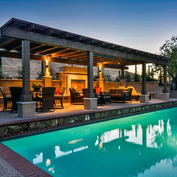 an outdoor living area with a pool and covered patio next to the swimming pool at dusk