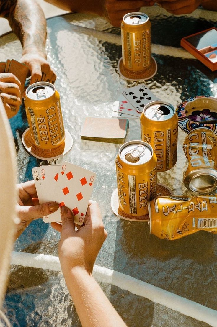 people playing cards and drinking beer at a table with other items on the glass top