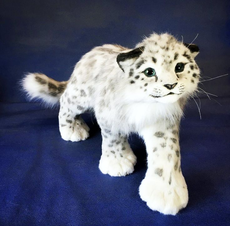 a stuffed snow leopard is standing on a blue surface and looking at the camera with one eye open