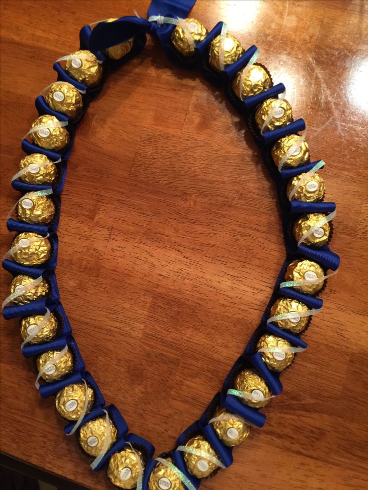 a necklace made out of gold and blue beads on a wooden table with a ribbon around it