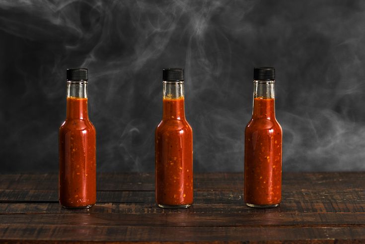 three bottles filled with hot sauce sitting on top of a wooden table