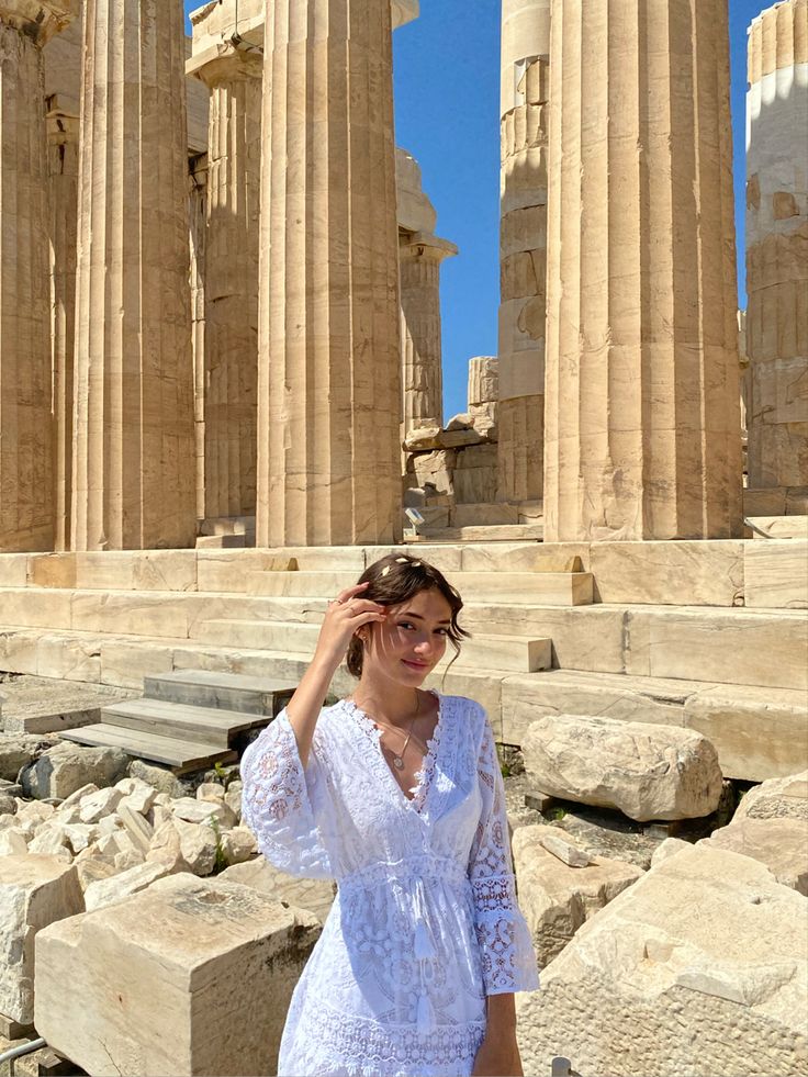 a woman is standing in front of the ruins of an ancient city with columns and pillars