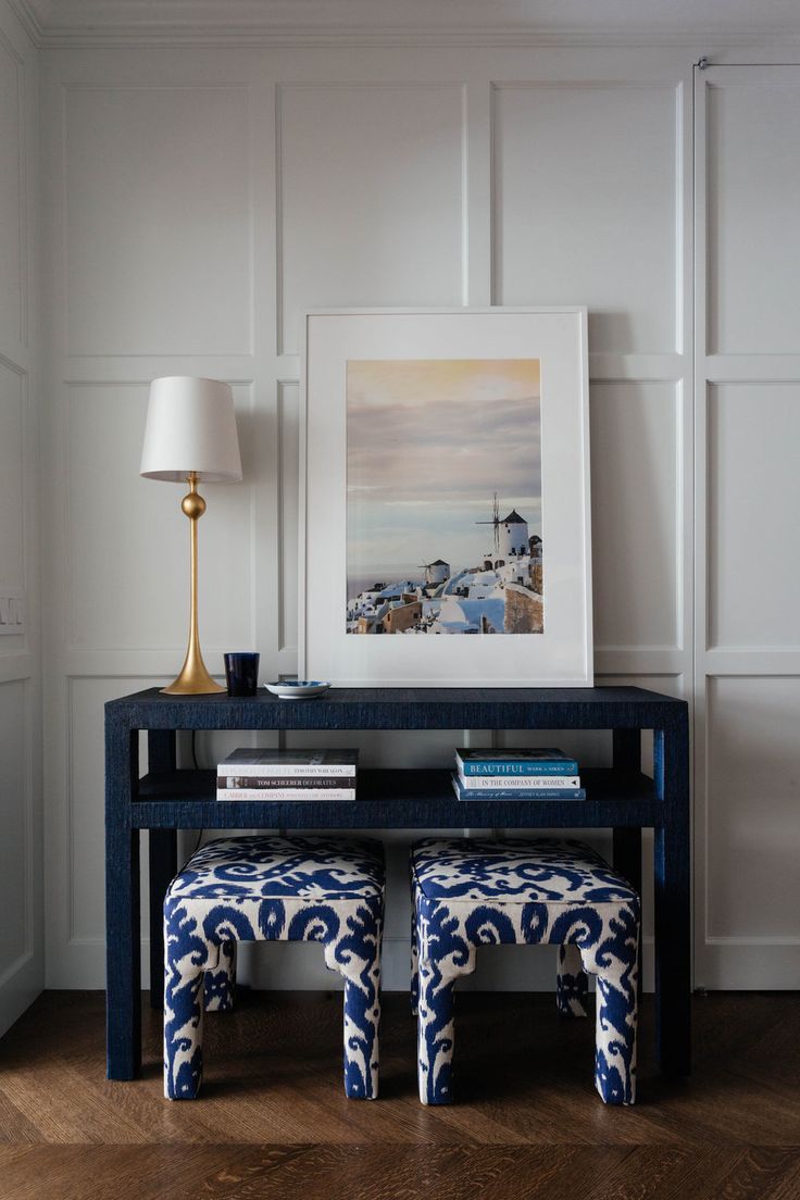 a blue table with two stools and a painting on the wall behind it in a white room