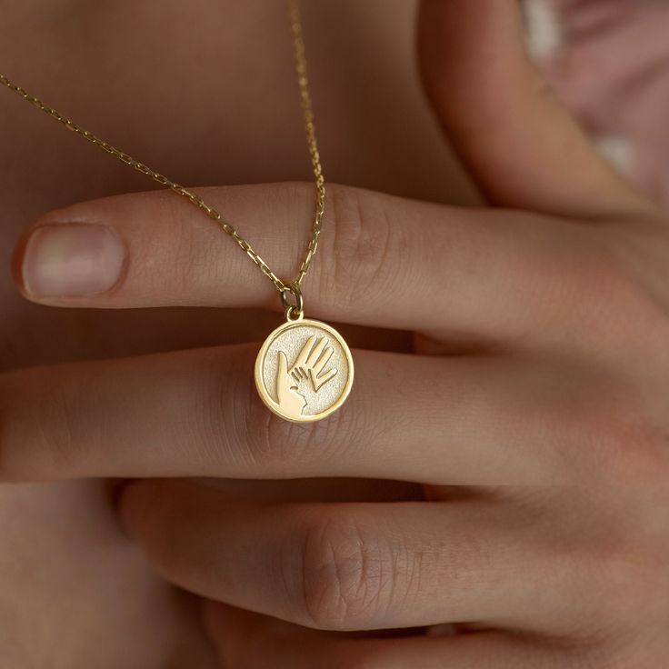 a woman's hand holding a gold necklace with a small round pendant on it