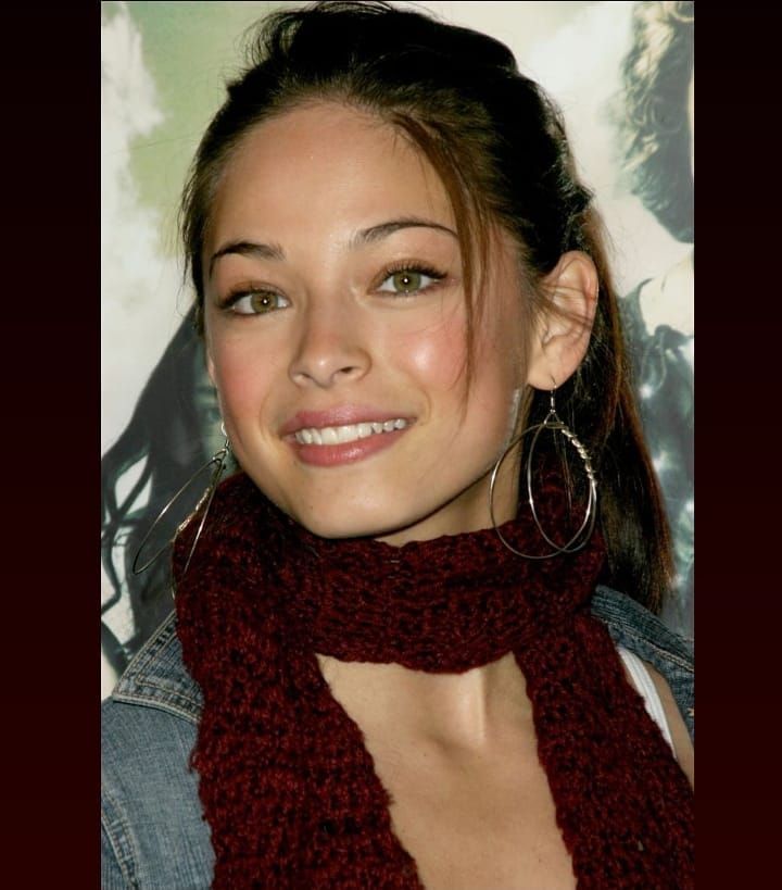 a close up of a person wearing a scarf and smiling at the camera with an earring on