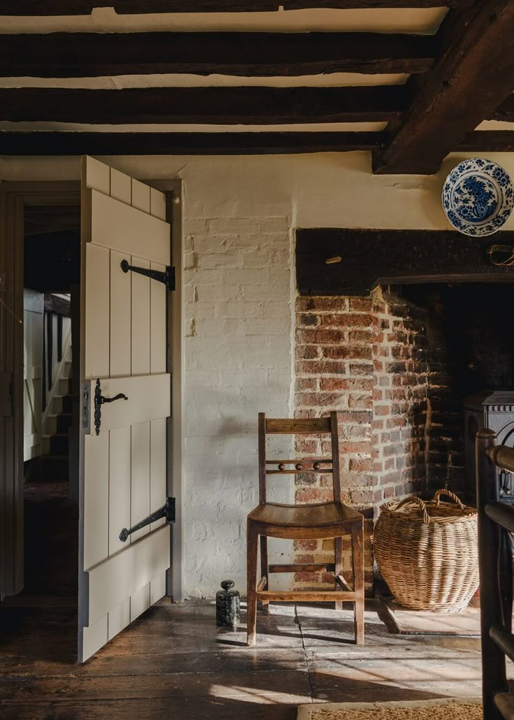 an old chair sitting in front of a brick wall with a basket on the floor next to it