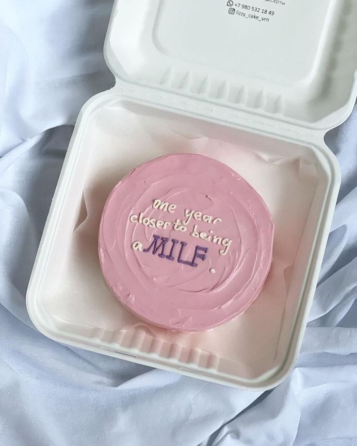 a pink frosted cake in a plastic container with writing on the top and bottom