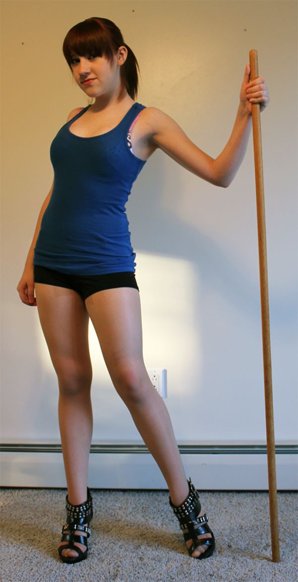 a woman is posing with a pole in front of a wall and wearing short shorts