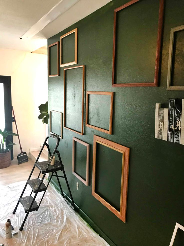 a green wall with several frames on it and a stepladder in the foreground