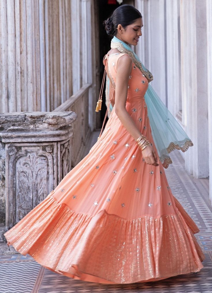 This look features a tangerine anarkali gown set. The v neck, sleeveless anarkali is embellished with gold sequin and mirror embroider. It further descends into a thick sequin & thread embroidered border. A contrast mint net dupatta with a scallop border and bootis completes the look. Cancan & pockets are included. Composition: Anarkali - Viscose georgette ,Dupatta - Soft net Care: Dry Clean Only and Vacuum Storage This product can be customised for colour, sleeves, length of blouse and neck des Semi-stitched Sleeveless Anarkali Set With Mirror Work, Bollywood Style Sleeveless Embellished Anarkali Set, Sleeveless Mirror Work Anarkali Set For Festive Occasions, Sleeveless Anarkali Set With Mirror Work For Festive Occasions, Sleeveless Anarkali Dress With Gota Work, Sleeveless Anarkali Set With Mirror Work For Festivals, Festive Sleeveless Anarkali Set With Mirror Work, Anarkali Style Lehenga With V-neck And Resham Embroidery, Traditional Sleeveless Embellished Anarkali Set