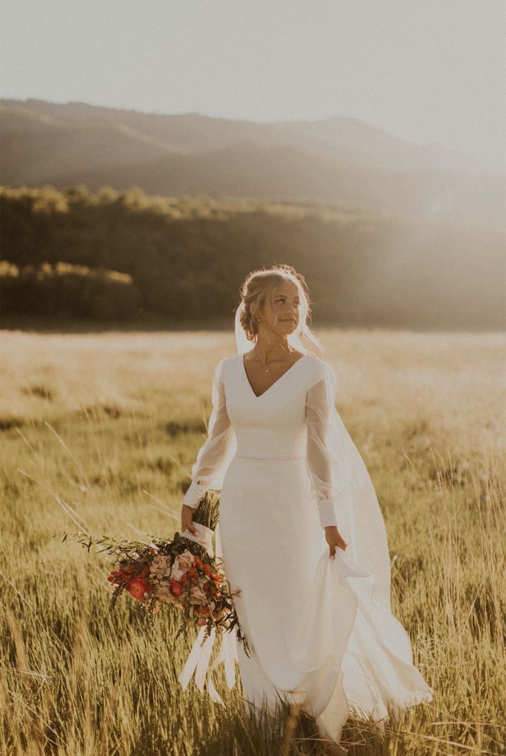 a woman in a white dress is standing in the grass with her bouquet and looking at the camera