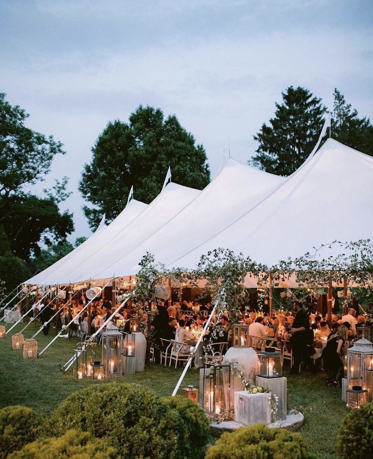 a large tent set up with tables and chairs for an outdoor wedding reception at dusk