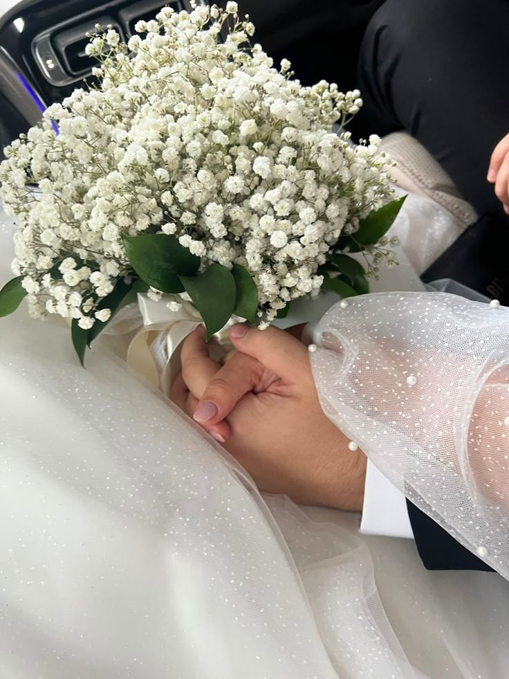 a bouquet of white flowers is being held by a bride in the back seat of a car