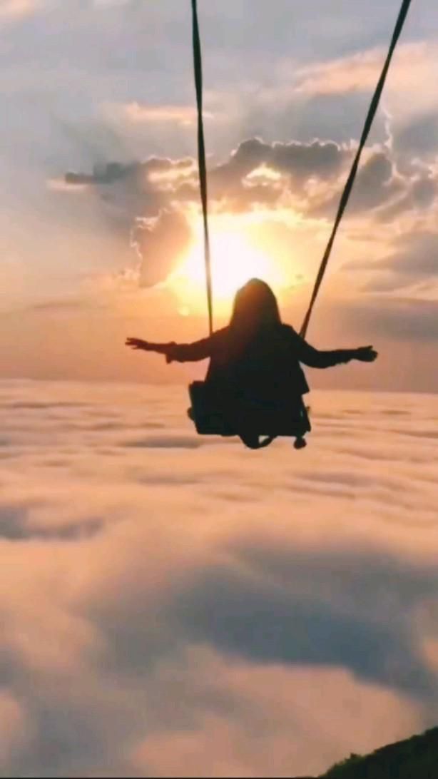 a person is flying through the air on a swing in the sky with clouds below