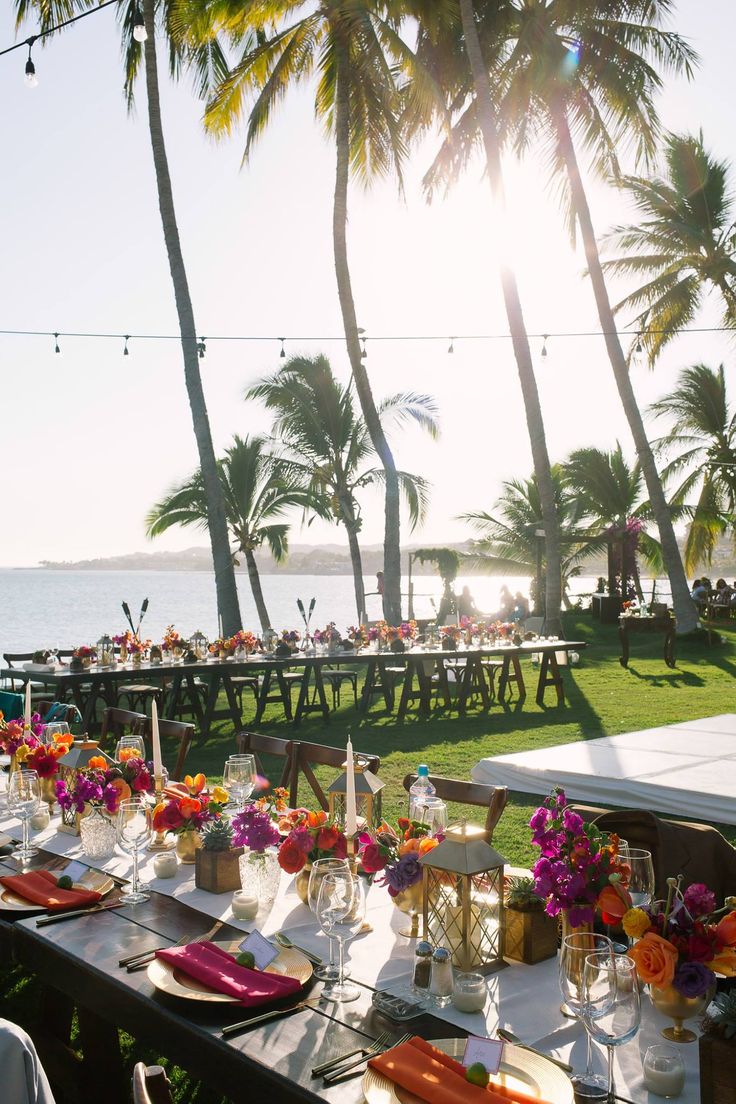 a long table set up with place settings for an outdoor dinner on the lawn next to the ocean