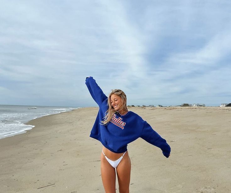 a woman standing on top of a sandy beach next to the ocean with her arms in the air