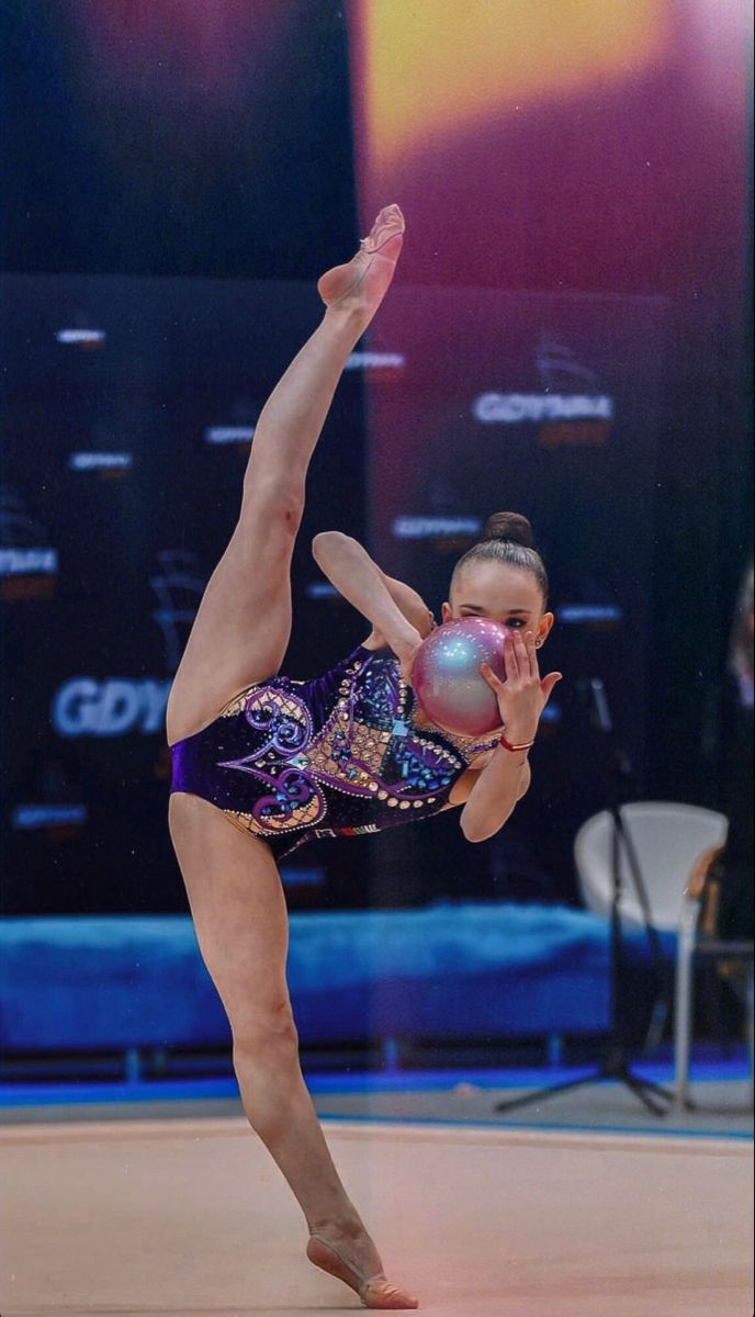 a woman is doing a trick on the floor with her hands in the air while wearing a purple and blue leotard