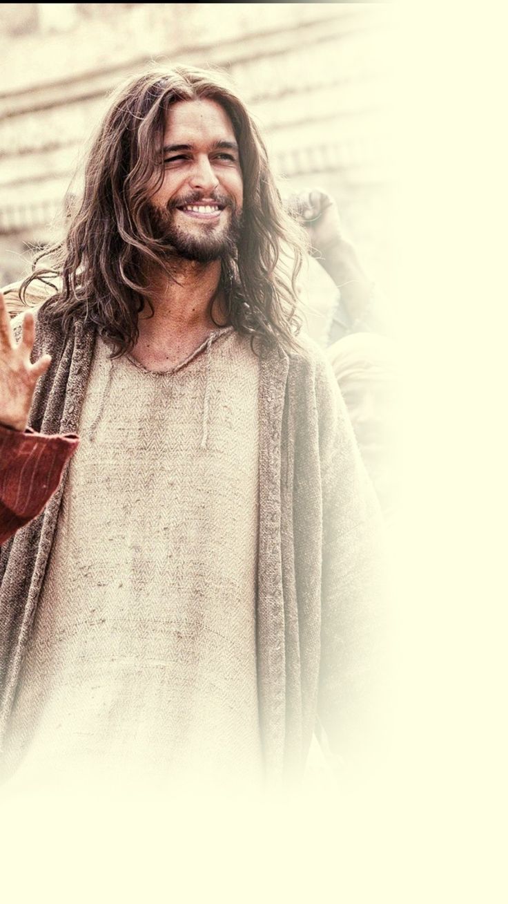 a man with long hair and beard standing in front of a building holding his hands up