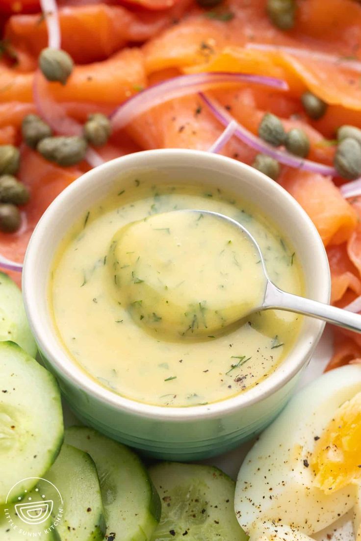 a bowl filled with dressing next to sliced cucumbers and carrots