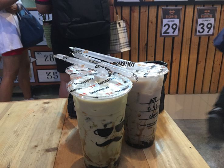 two iced drinks sitting on top of a wooden table next to people in the background