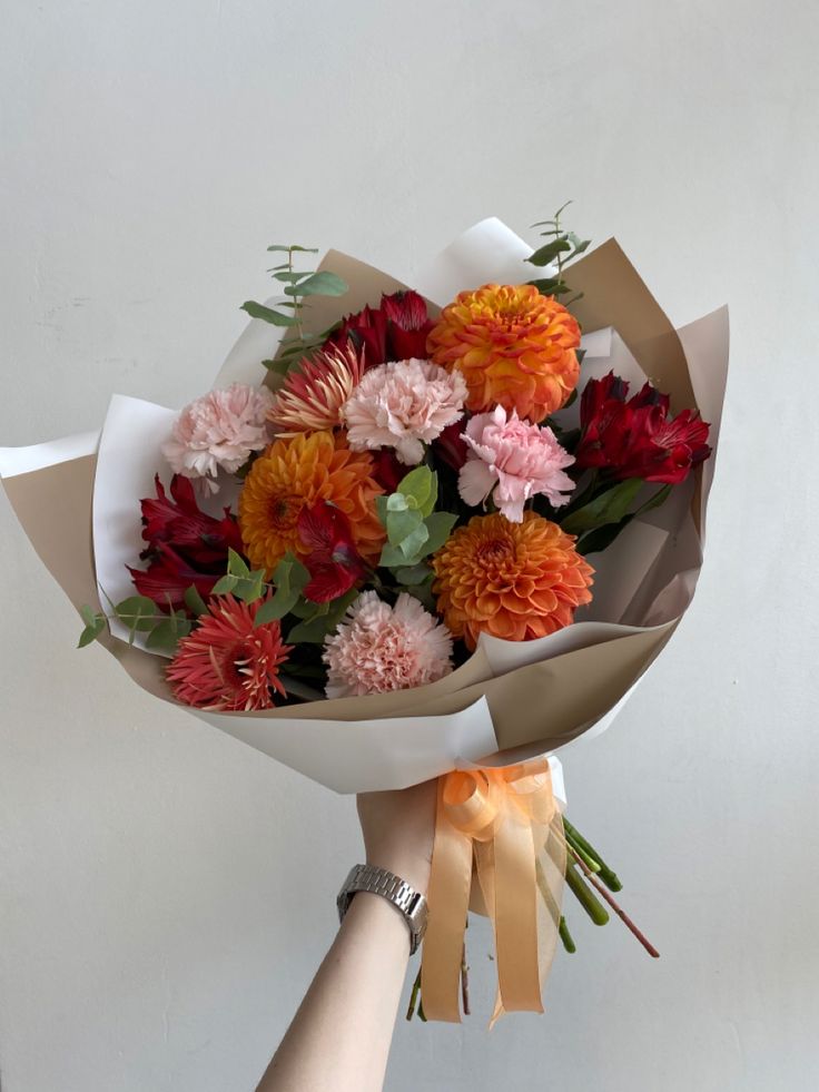 a bouquet of flowers is being held by someone's hand in front of a white wall