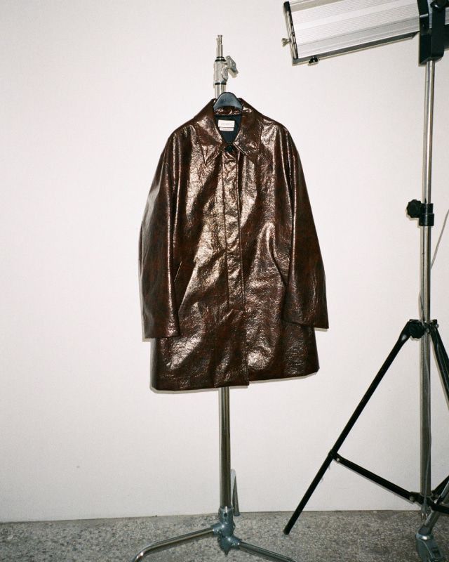 a brown leather coat is hanging on a tripod in front of a white wall