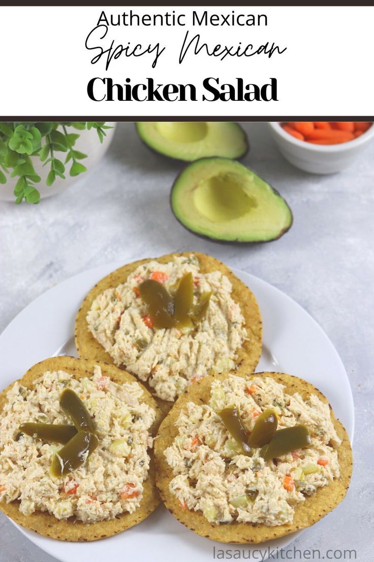 three chicken salad sandwiches on a white plate with avocado and carrots in the background