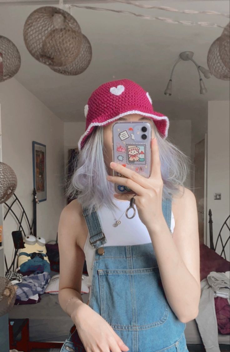 a woman with grey hair wearing overalls and a pink hat taking a selfie