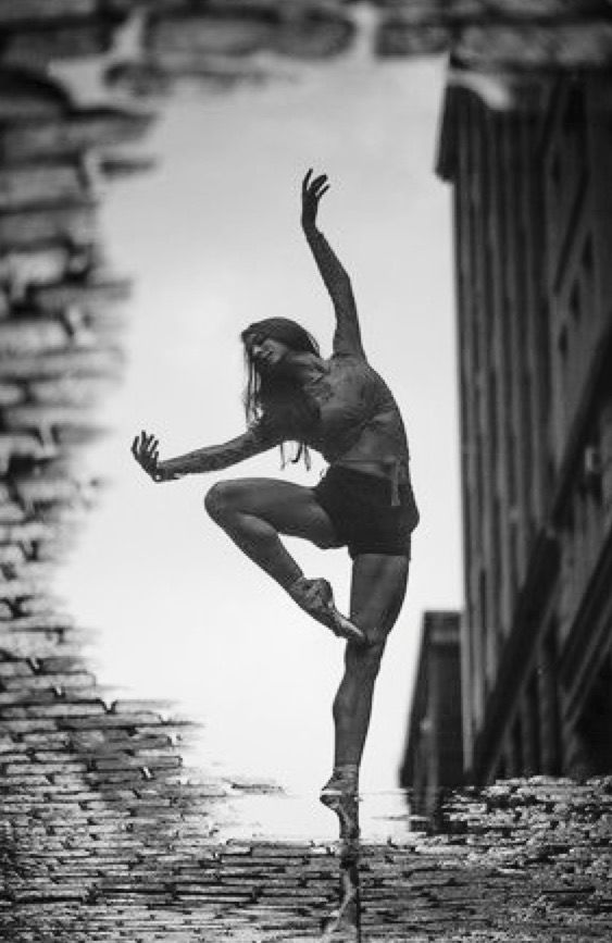 a woman is dancing in the rain on a ledge with her arms outstretched and legs spread out