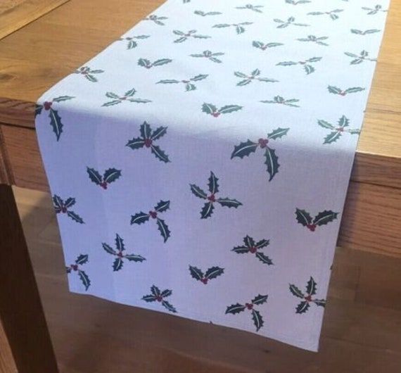 a white table with holly leaves on it and red berries on the top is sitting next to a wooden table