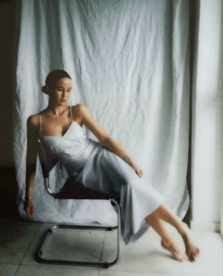 a woman sitting on a chair in front of a white curtain