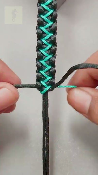 two hands holding a piece of string with green and blue yarn on it, while another person holds the string in their hand