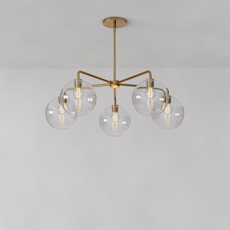 three clear globes hanging from a brass chandelier with four bulbs on each end