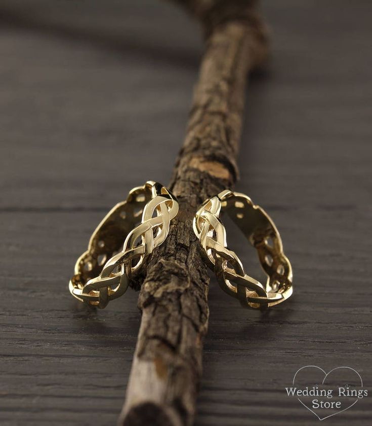 two gold rings sitting on top of a piece of drift wood next to a twig