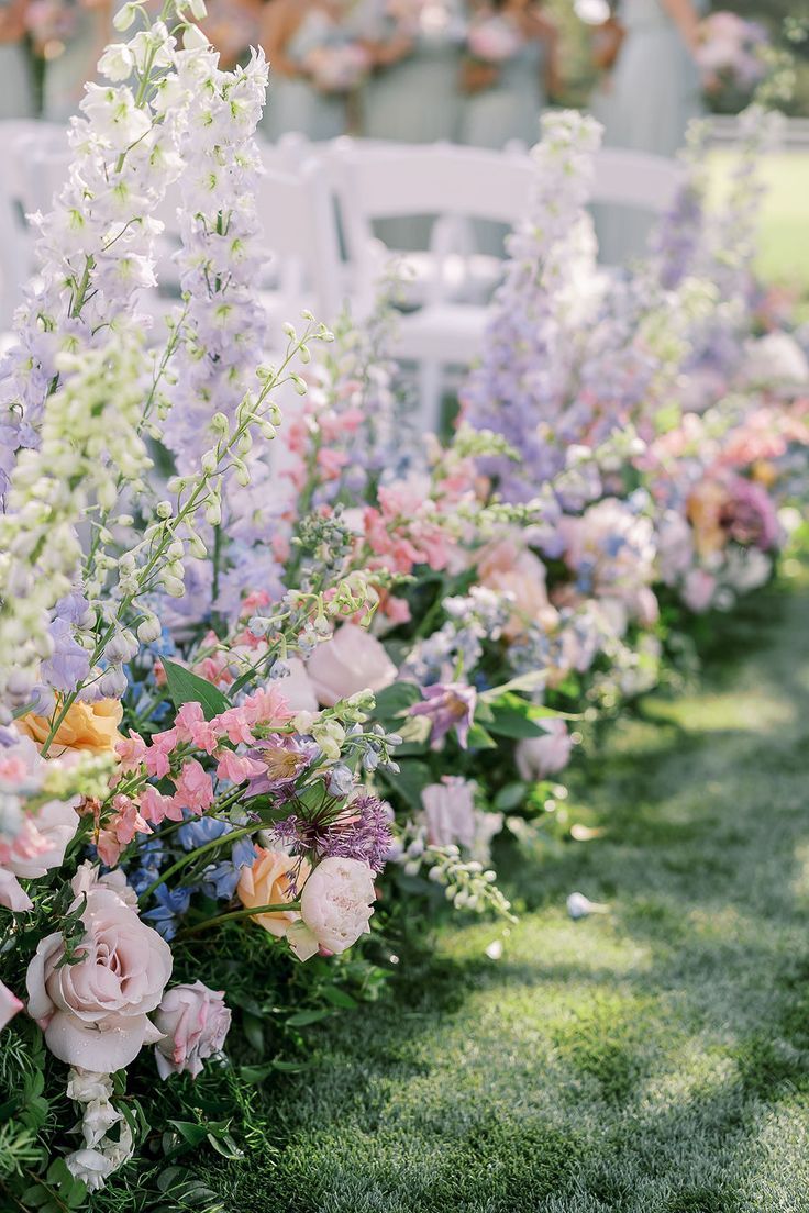 rows of white chairs with pink and blue flowers lining the aisle at a wedding ceremony