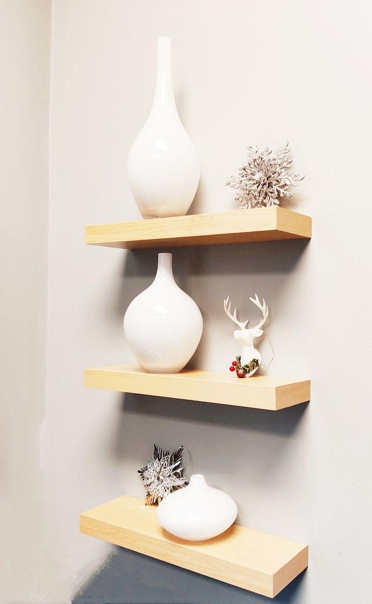 three wooden shelves with white vases and other decorative items on them in a corner